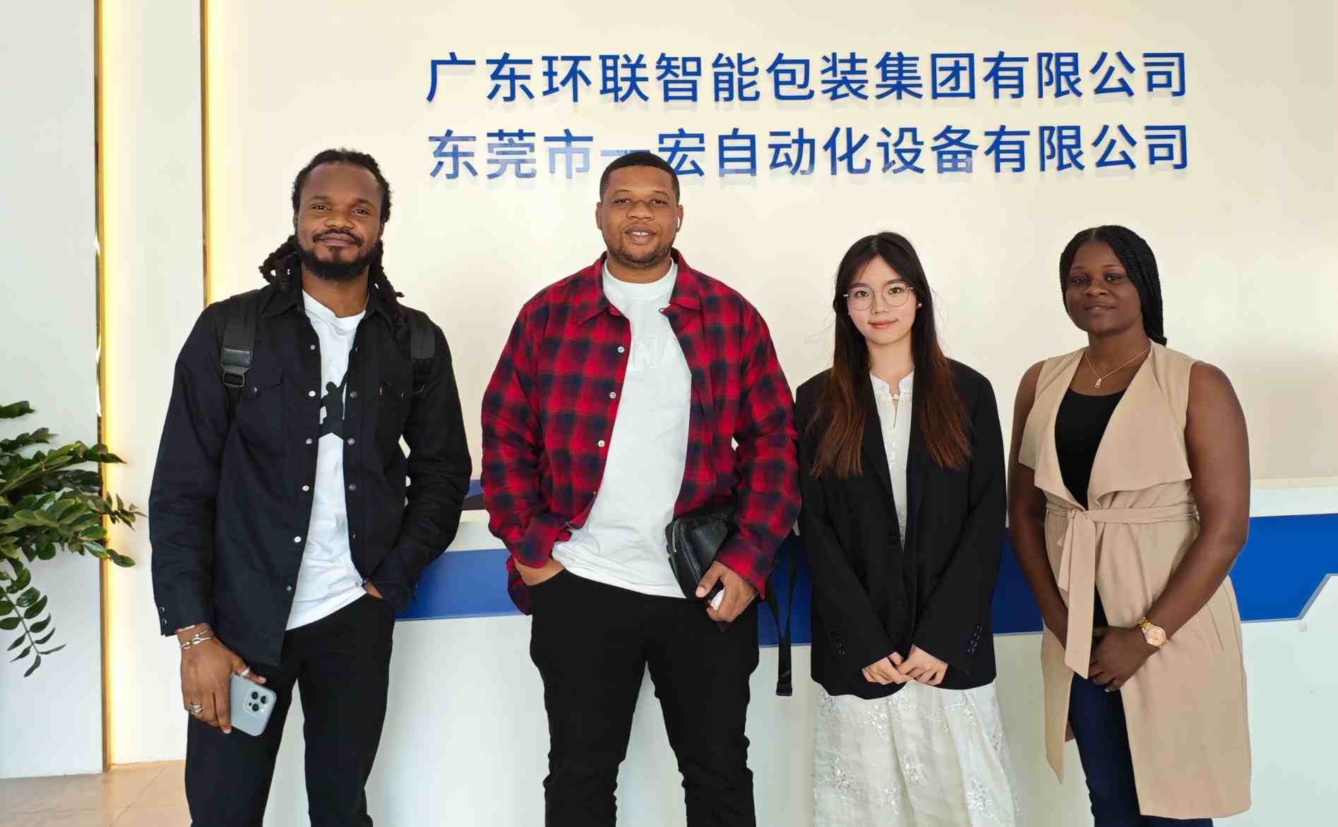 UBL sales team posing for a photo with Malaysian clients at the front desk area, with the signage of Guangdong UBL Intelligent Packaging Group and Dongguan Yihong Automation Equipment Co., Ltd. displayed in the background