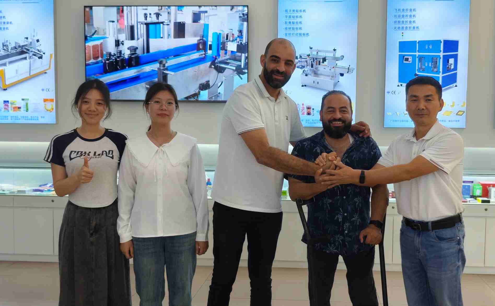 UBL’s Brazilian clients posing for a photo with staff members in the equipment exhibition hall: The group (including the Brazilian clients and UBL team) gathers together, with handshakes and thumbs-up gestures showing positive collaborative rapport; equipment display posters are visible in the background