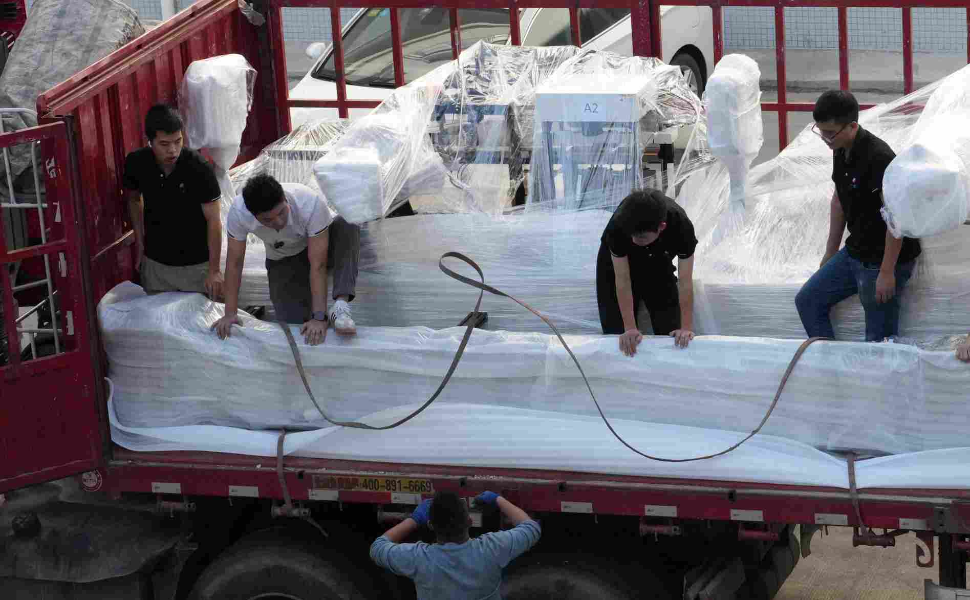 UBL’s equipment loading operation: Staff members are securing packaged intelligent packaging equipment (wrapped in protective materials) on the bed of a delivery truck, properly fastening the cargo to ensure safe transportation