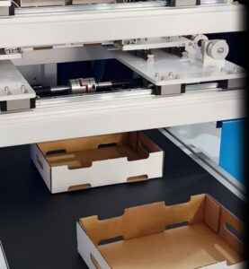 An automatic rigid box lid-and-base folding machine in operation, assembling boxes on a running conveyor system.