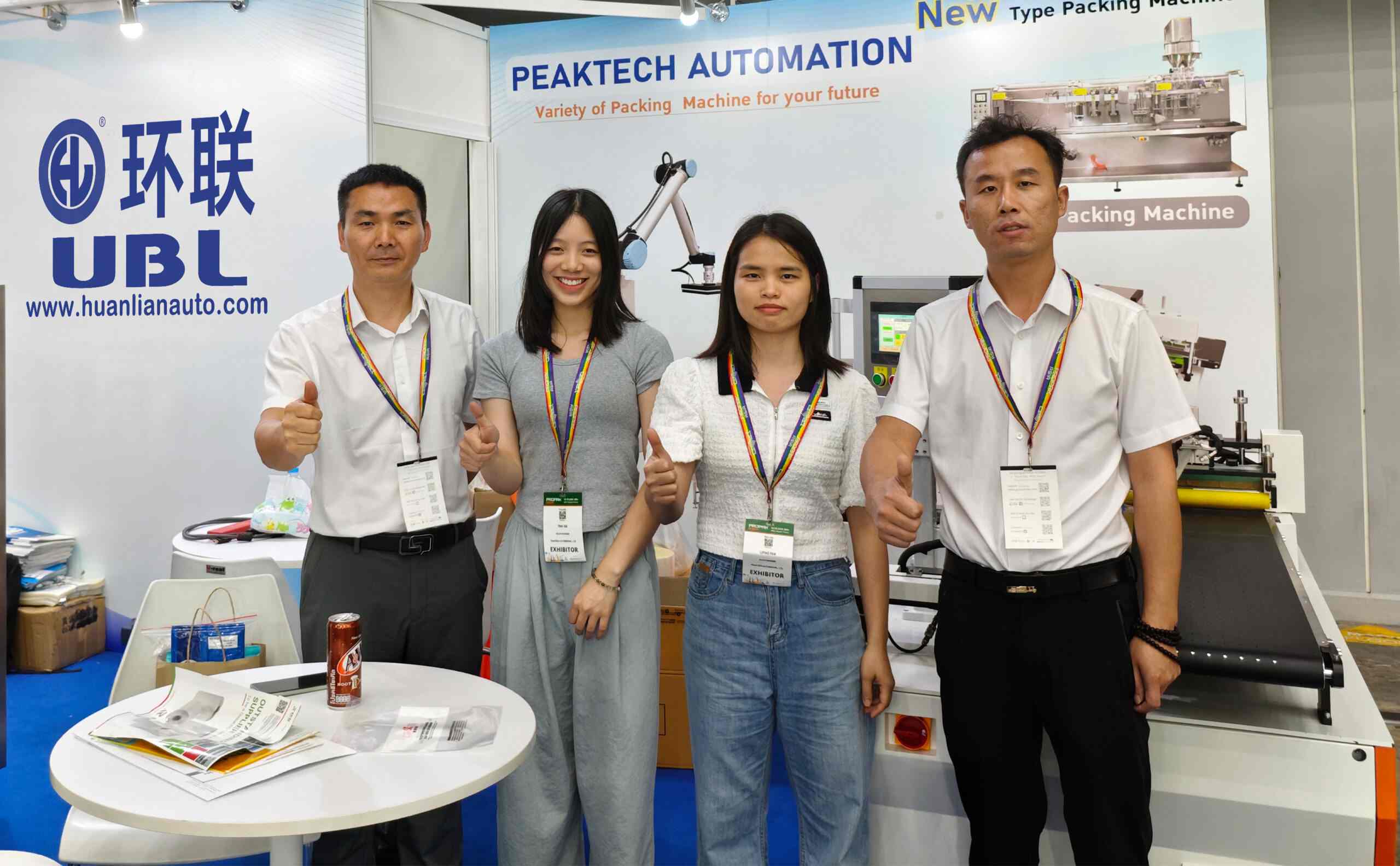 UBL (Huanlian Packaging Group) team at a trade show booth with UBL branding: Co-exhibiting with PEAKTECH AUTOMATION to present various packaging machines, with our staff posing at the exhibition stand