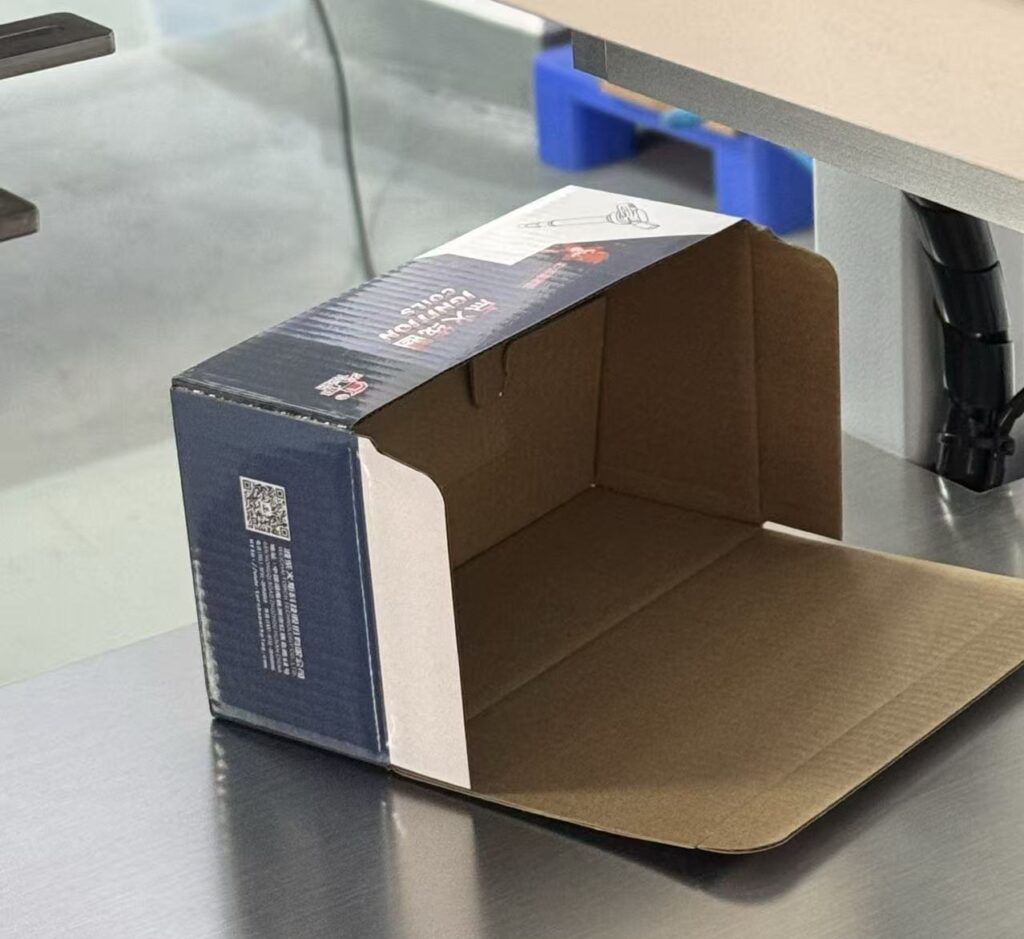 Open e-commerce corrugated packaging box placed on a cartoning machine’s stainless steel platform — used in e-commerce supply chain packaging lines for automatic box forming
