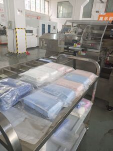 Finished products of the fully automatic bagging machine: Packaged towels are neatly arranged on a metal cart. In the background, the bagging equipment marked "demonstration machine" is situated in the workshop display area.