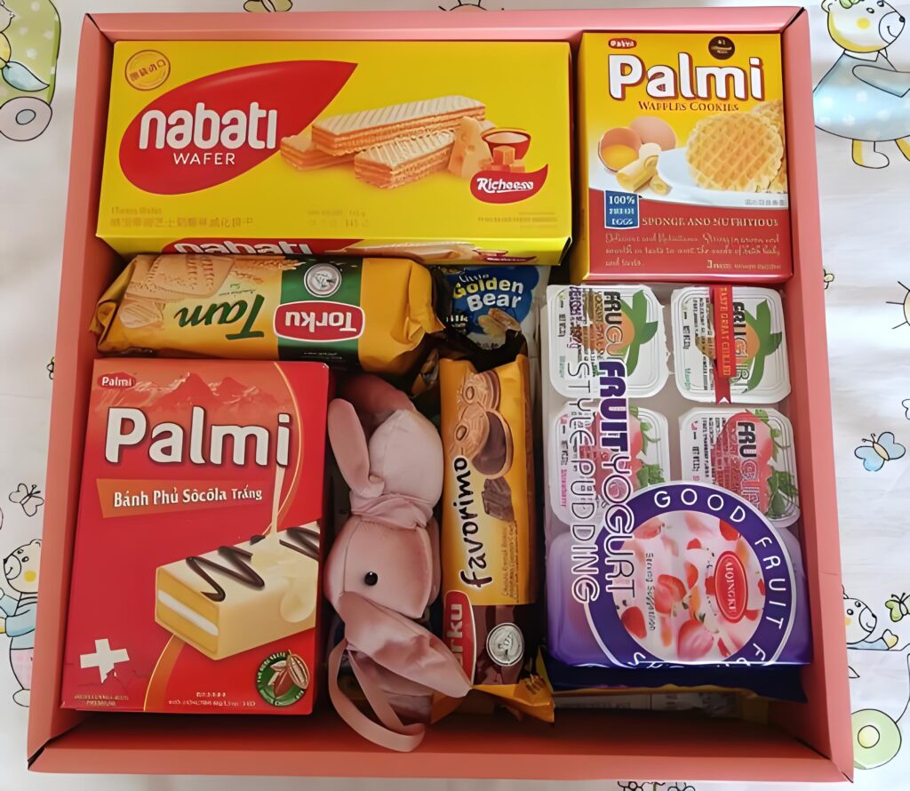 A pink gift box filled with assorted snacks (including Nabati wafers, Palmi treats, and yogurt puddings) — these neatly packaged food items showcase the consistent, appealing appearance enabled by Food Packaging Machinery, which ensures professional, consumer-friendly packaging for various snack products.