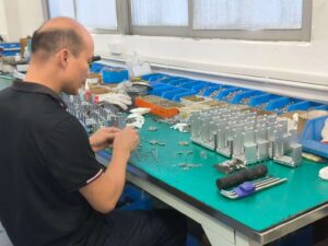 A factory worker performing manual packaging of precision metal hardware components at an assembly workbench.