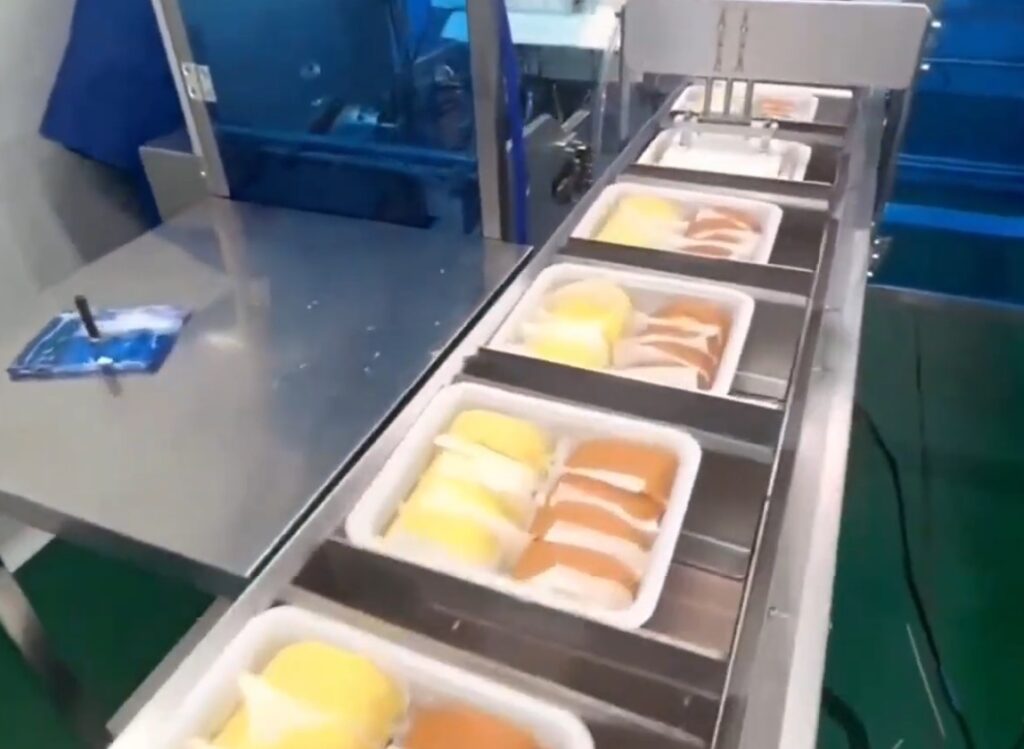 Automated food packaging line with conveyor system, efficiently processing pre-packed meal containers