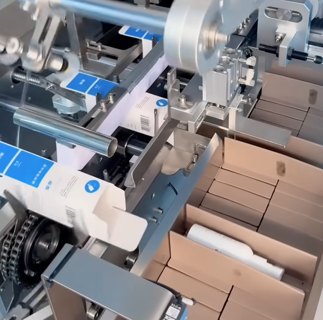 Automatic cartoning machine in operation, packaging blue-and-white personal skincare products into cardboard boxes on an industrial production line