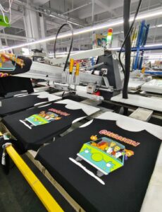 Automatic screen printing production line for black T-shirts with Scooby-Doo cartoon prints, showing high-volume apparel manufacturing process in a factory, ideal for automated garment folding and packaging workflows