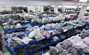 Hand-folded apparel inventory neatly arranged on blue shelves in a warehouse, showing organized finished garments with high-quality manual folding, ready for packaging and shipping
