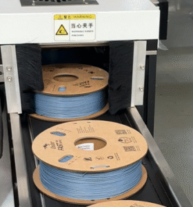 Finished 3D printing filament spools exiting the Spool Packaging Machine after automated bagging
