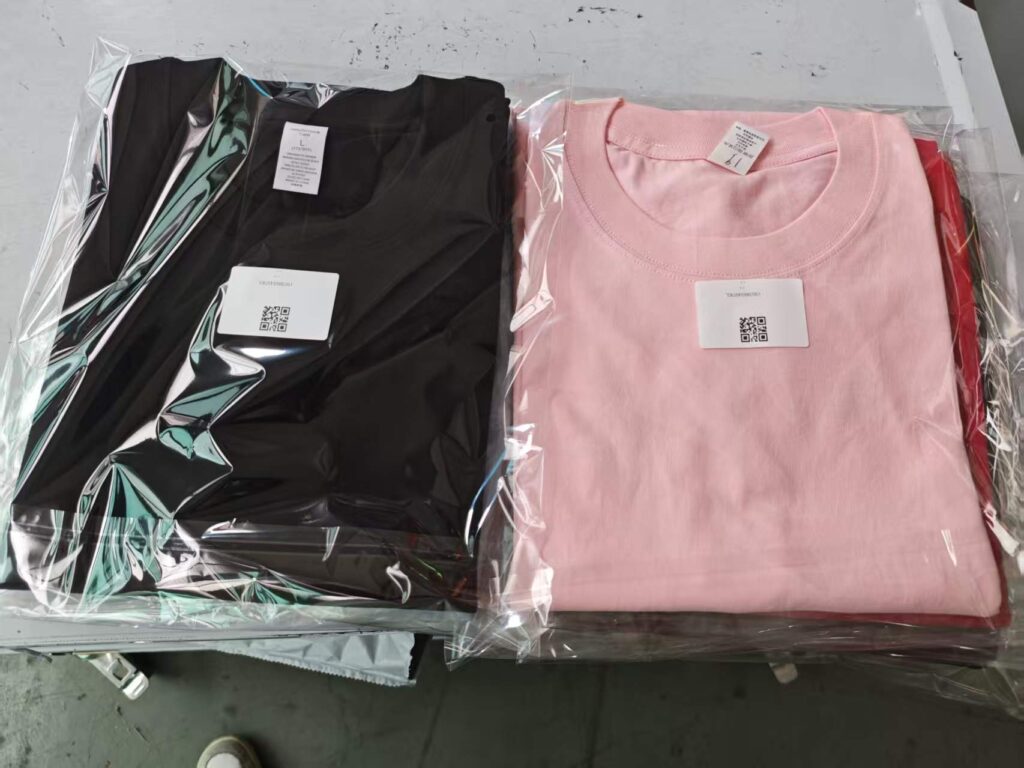 Folded and packaged t-shirts from a t-shirt folding machine, showing neatly packed apparel with tags and QR codes.