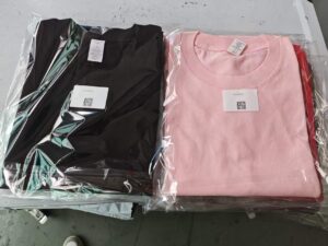 Folded and packaged t-shirts from a t-shirt folding machine, showing neatly packed apparel with tags and QR codes.