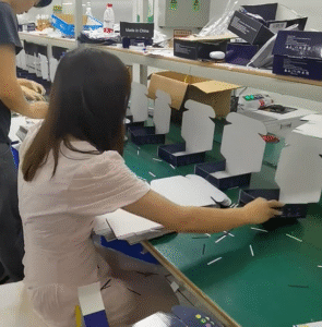 Workers manually folding corrugated mailer boxes (shipping mailer boxes) on an assembly line in a factory