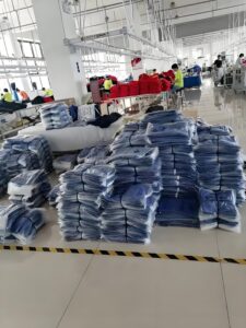 Garment factory production line with stacks of folded clothes ready for packaging, showing high-volume apparel processing that uses a clothes folding machine.