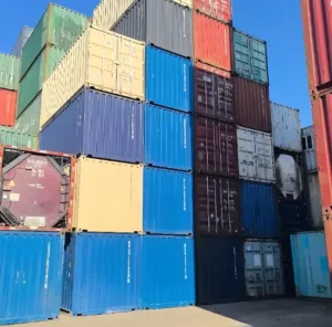 Stacked shipping containers representing ocean transport conditions, highlighting the risk of 'container rain' and humidity exposure that threatens 3D printing filament during long shipping cycles, leading to moisture absorption and print quality issues.